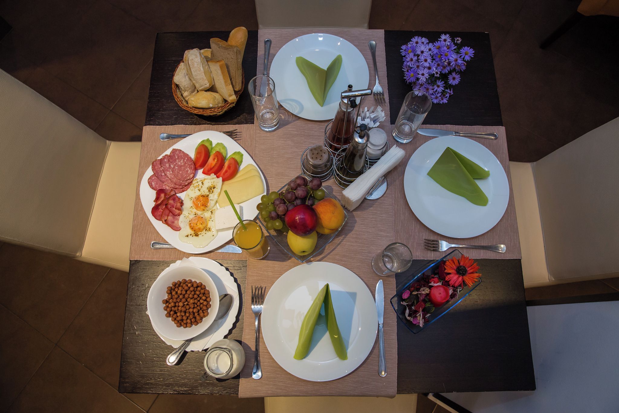 A breakfast table with plates of food, a bowl of nuts, and a basket of bread.