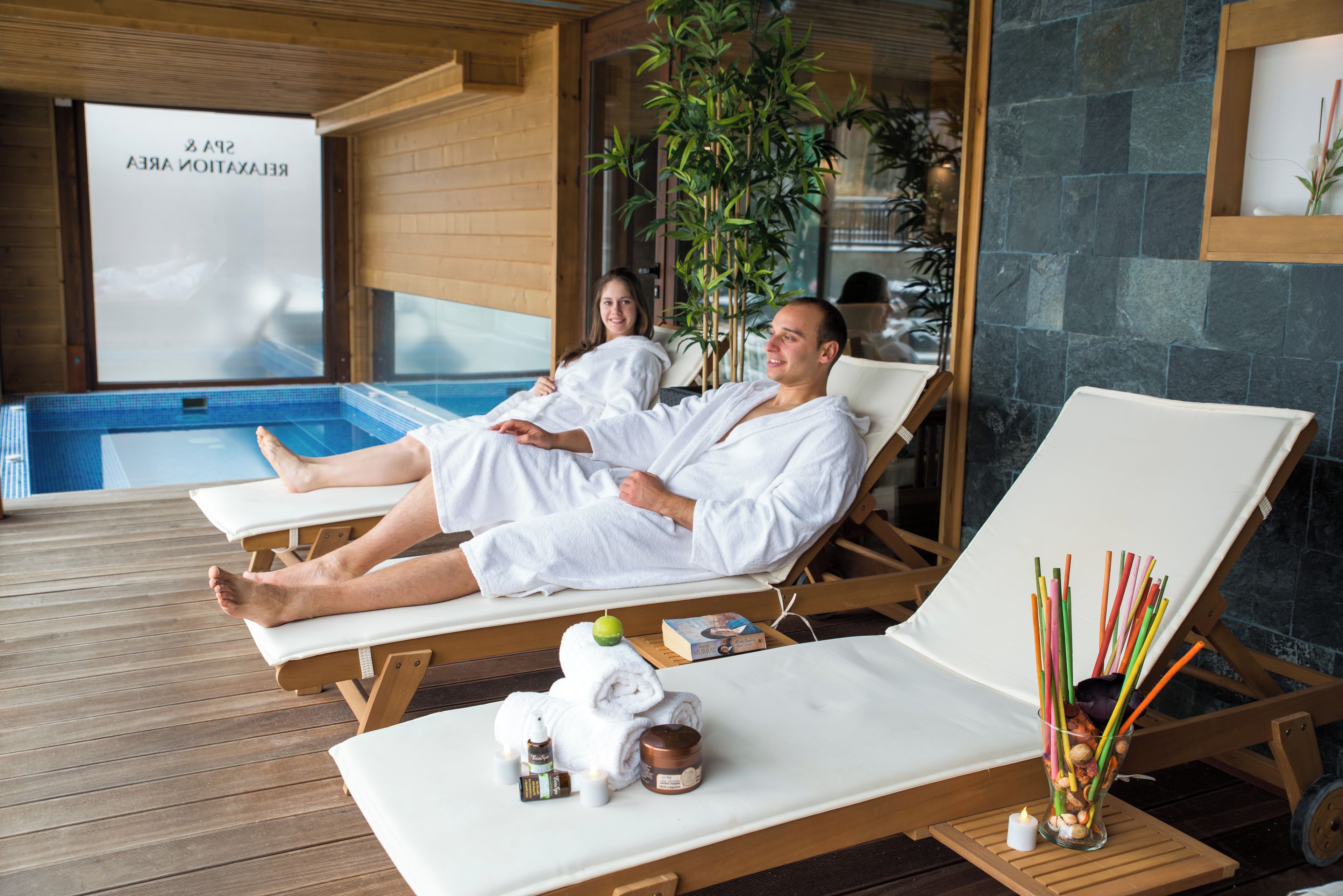 Un área de spa con tumbonas de madera, una piscina y una pared de vidrio con un letrero.