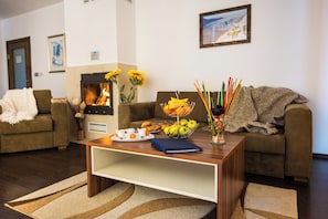 A living room with a fireplace, sofas, a coffee table with breakfast items, and a painting on the wall. - The Balkan Jewel Resort, Trademark Collection By W (Razlog)