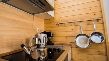 A compact kitchen with a coffee maker, kettle, and hanging pots on a rack.