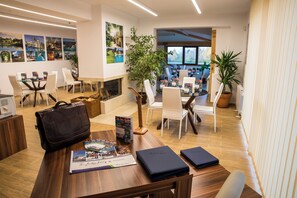Eine moderne Hotelhalle mit einem Holzbüro, weißen Stühlen, einem Kamin und einem großen Fenster mit Blick ins Freie.