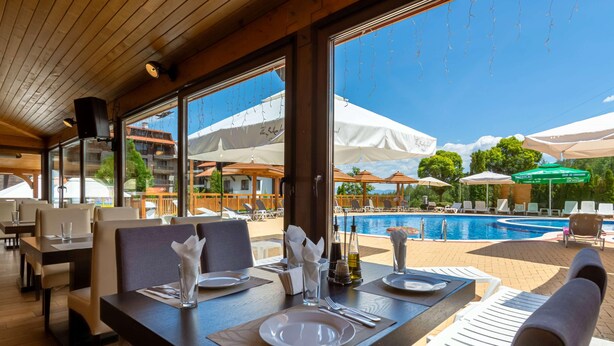Ein Restaurant mit gedeckten Tischen, ein Poolbereich ist durch die Fenster zu sehen, und Sonnenschirme im Außenbereich.