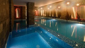 Ein Schwimmbad mit hellblauen Fliesen, umgeben von Wänden mit reflektierenden Oberflächen und roten Lichtakzenten.