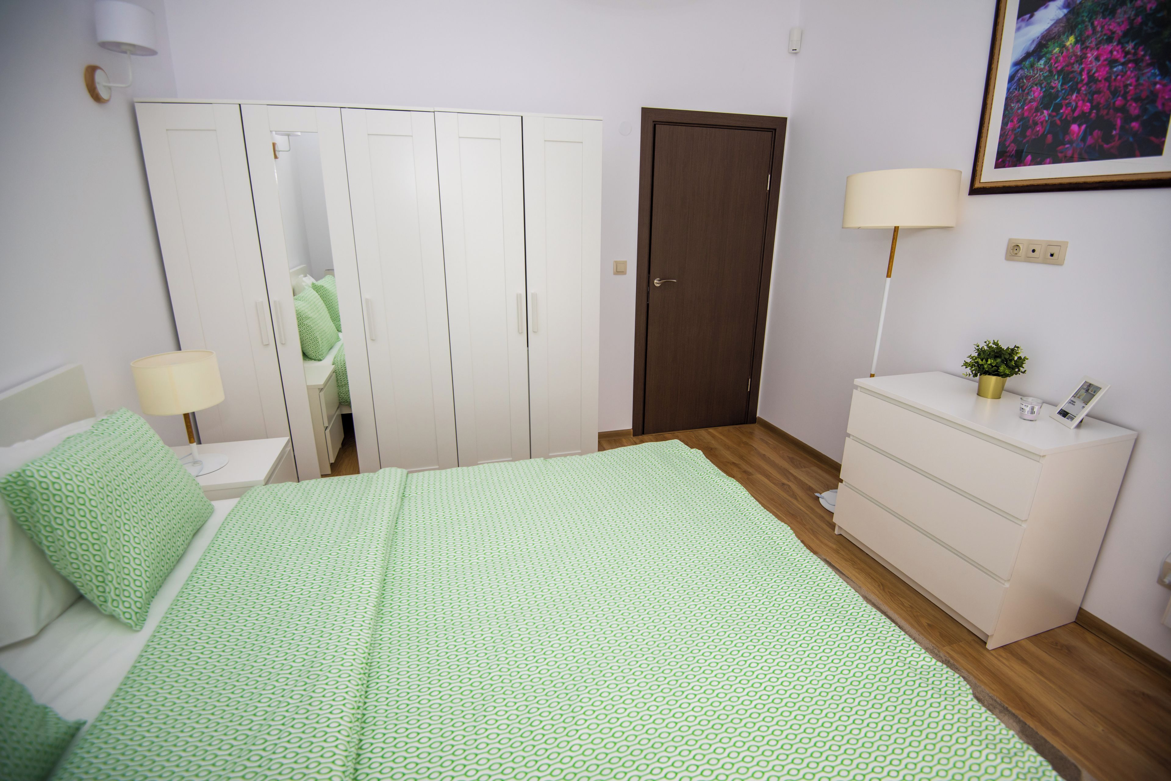 A bedroom with a bed, a dresser, a nightstand, a lamp, and a door.