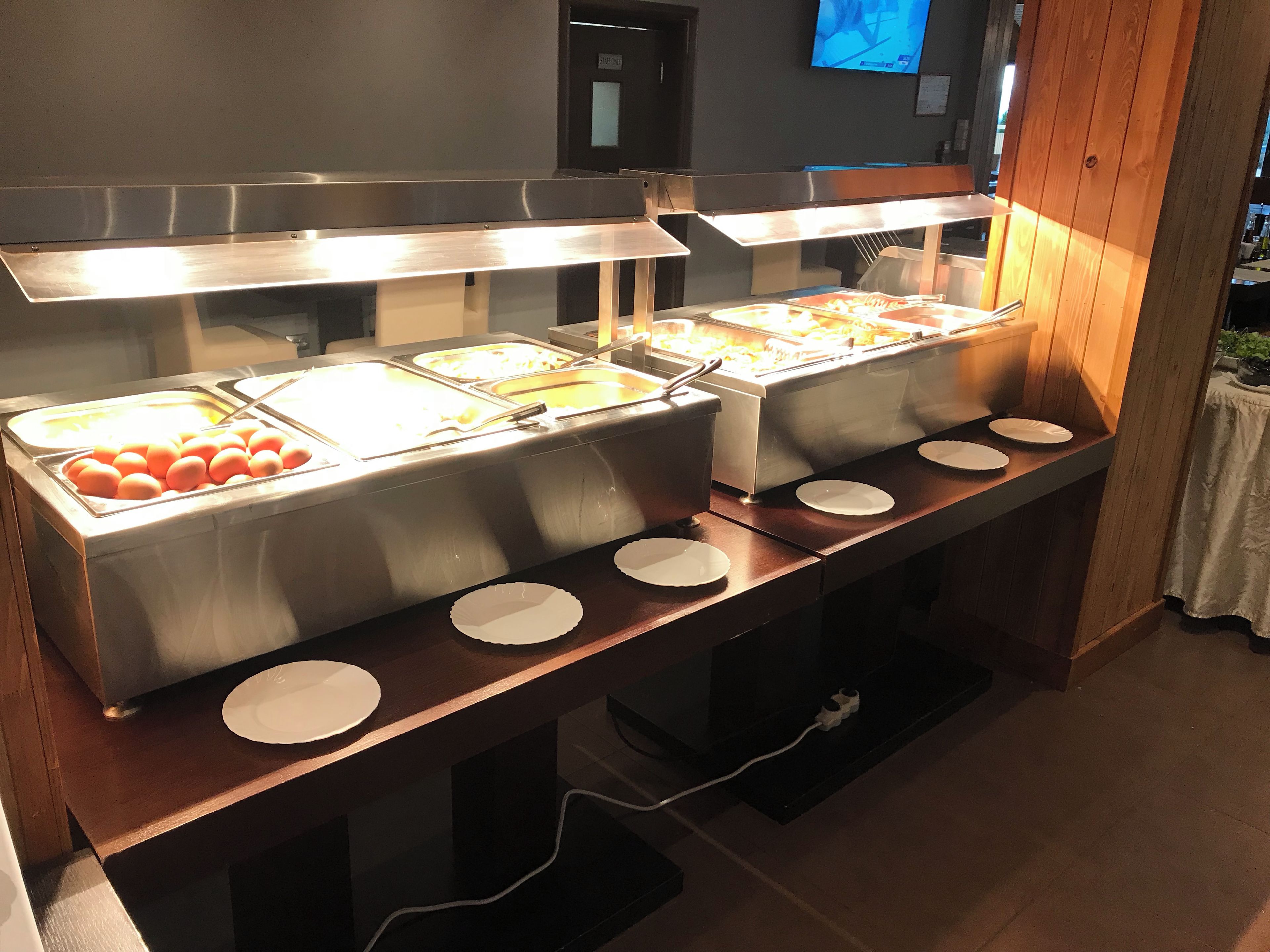 A buffet with multiple food stations, a television screen, and a wooden panel wall.