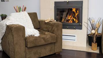 A brown sofa with a white throw blanket, a fireplace with a visible fire, and a small plant in a wooden pot.