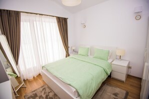 Ein Schlafzimmer mit einem Bett, Nachttischen, einer Lampe, einem Spiegel und Vorhängen.
