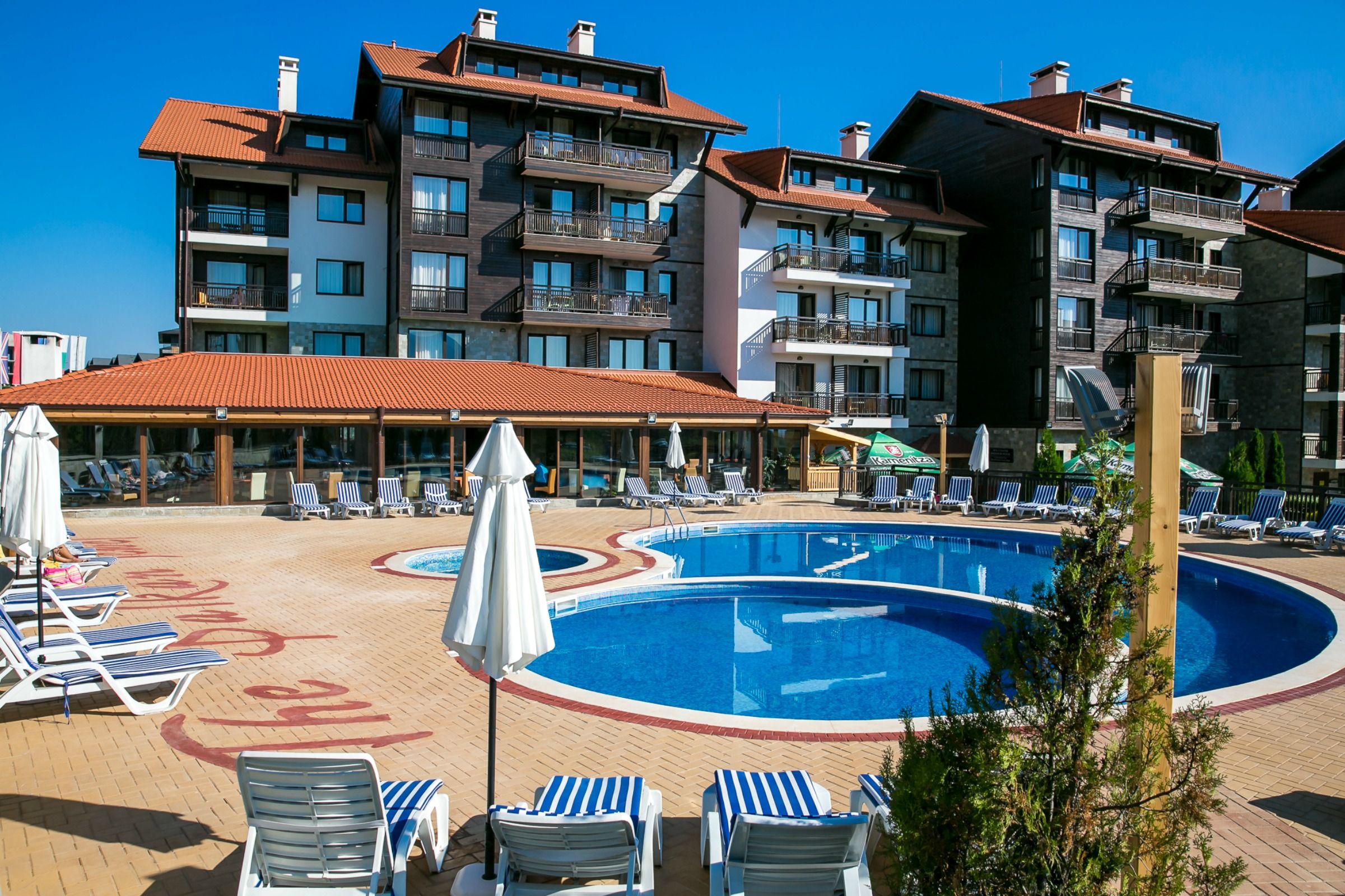 A pool area with lounge chairs and umbrellas, surrounded by multi-story buildings with balconies.