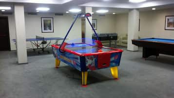 A pool table, a foosball table, and a ping pong table in a room with a carpeted floor and white walls.
