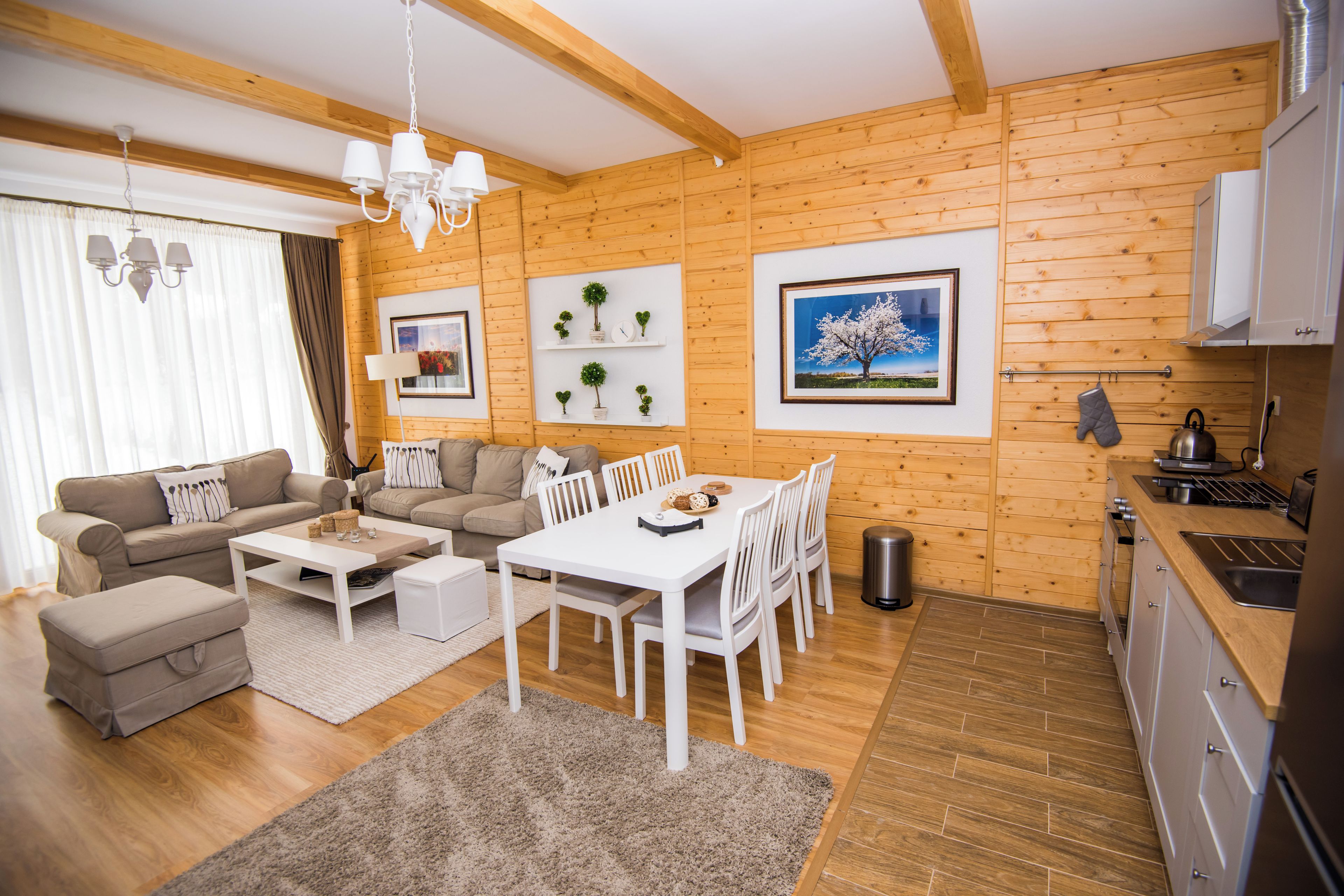 Una sala moderna con sofá, una mesa de comedor con sillas, una cocina con pileta y estufa, y paredes de madera.