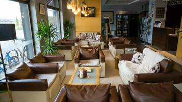 A hotel lobby with leather sofas, a reception desk, a coffee table, and a large window with a bicycle outside.
