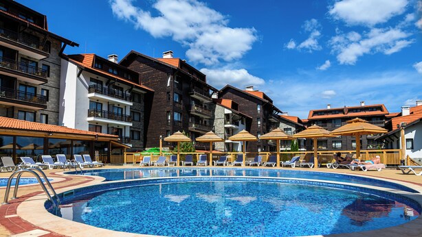 Une piscine entourée de chaises longues et un immeuble à plusieurs étages doté de balcons.