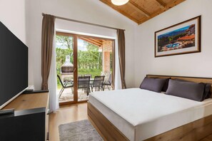 Une chambre avec un lit, une télévision et une porte-fenêtre coulissante donnant sur un espace extérieur aménagé avec une table et des chaises.