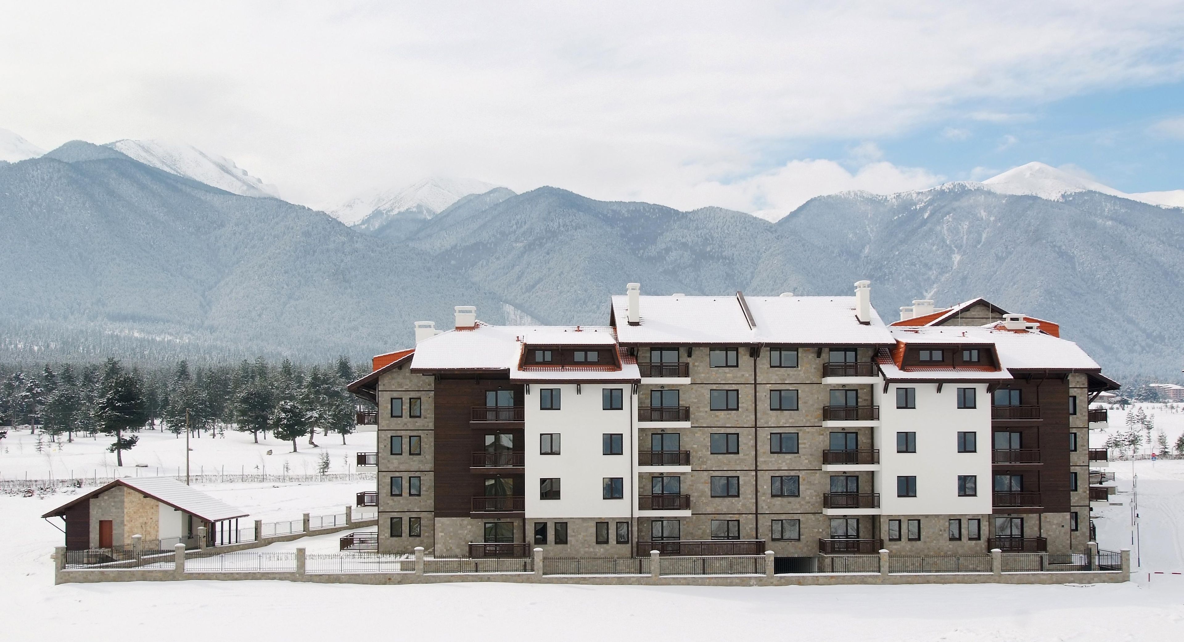 A multi-story hotel with balconies, a snow-covered landscape, and mountains in the background.