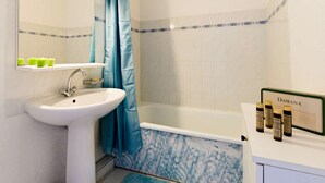 A bathroom with a white sink, a bathtub with a marble surround, a blue shower curtain, and a shelf with bottles labeled "Damana".