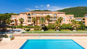 A hotel with a swimming pool, palm trees, and a mountainous backdrop.