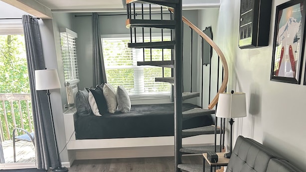 Una sala de estar moderna con una escalera curva, un sofá, una mesa de centro y vistas al exterior.