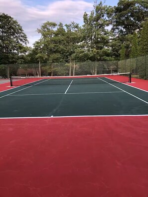 Una cancha de tenis con una red en el centro, rodeada de árboles y una valla.