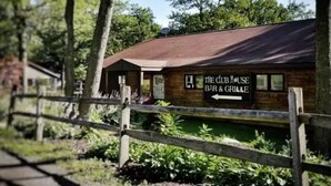 Un edificio de madera rústico con fachada de ladrillo y techo de metal, identificado con un letrero que dice 'The Club House Bar & Grill'.