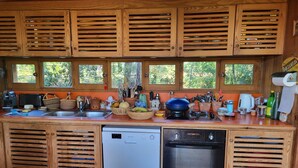 Une cuisine compacte avec des meubles en bois, un lave-vaisselle, un four encastré et une fenêtre donnant sur un espace verdoyant.
