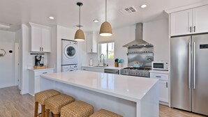 Een moderne keuken met een centraal eiland, roestvrijstalen apparatuur en geweven krukken.