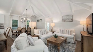 A spacious living area with a high ceiling, a dining table with chairs, a sofa set, a coffee table, and a television. - Dog Friendly, Heated Pool, Hot Tub, 5Min to Beach! (Southern Shores)