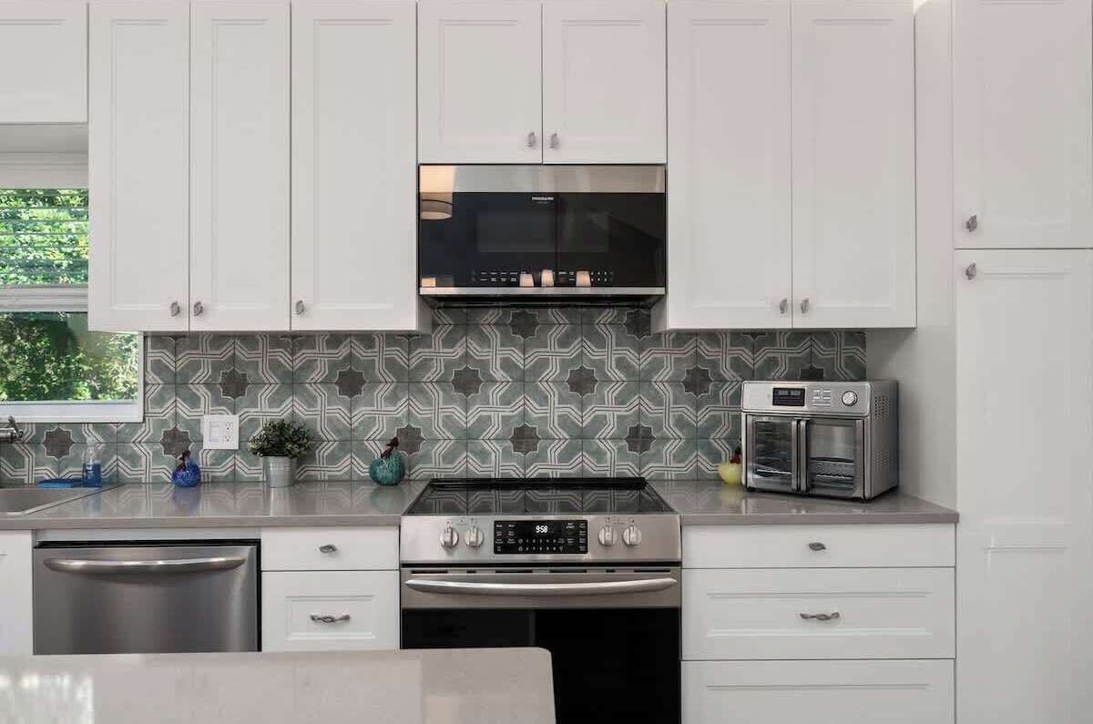 Una cocina moderna con gabinetes blancos, lavavajillas de acero inoxidable, horno empotrado, microondas y tostadora.