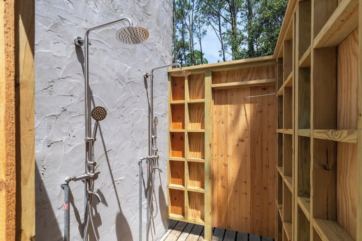A wooden outdoor shower with metal fixtures, a white textured wall, and a wooden deck.