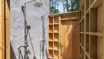 A wooden outdoor shower with metal fixtures, a white textured wall, and a wooden deck.