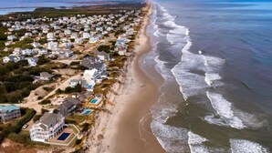 An aerial view of a coastal residential area with houses along the beachfront, a sandy beach, and the ocean.
