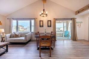 A spacious room with a dining table, chairs, a sofa, and a large window with a view. - Oceanside - Dog Friendly - Hot Tub (Kill Devil Hills)