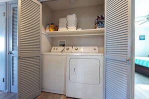 A laundry room with a washing machine and dryer, a shelf with folded towels, and a small window.