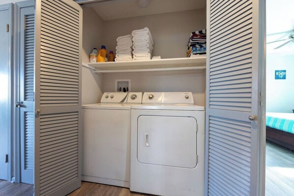A laundry room with a washing machine and dryer, a shelf with folded towels, and a small window. - Oceanside - Dog Friendly - Hot Tub (Kill Devil Hills)