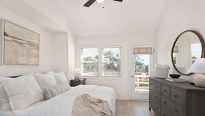 Un dormitorio con cama, mesita de noche, cómoda y un espejo grande. Hay una ventana con persianas y vistas al exterior.