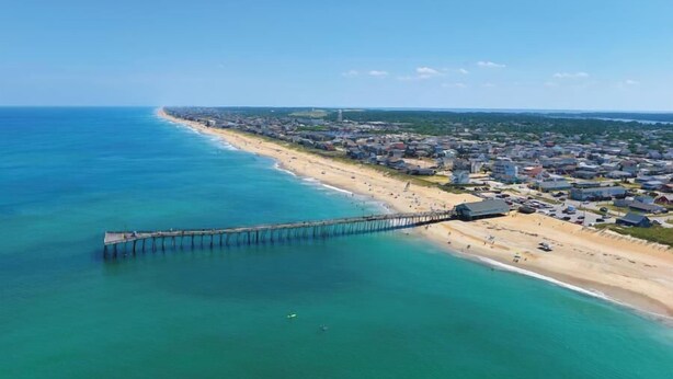 Vue aérienne d’une ville côtière avec une jetée qui s’avance dans la mer, une plage et des immeubles d’habitation.