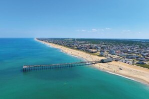 An aerial view of a coastal town with a pier extending into the sea, a beach, and residential buildings.