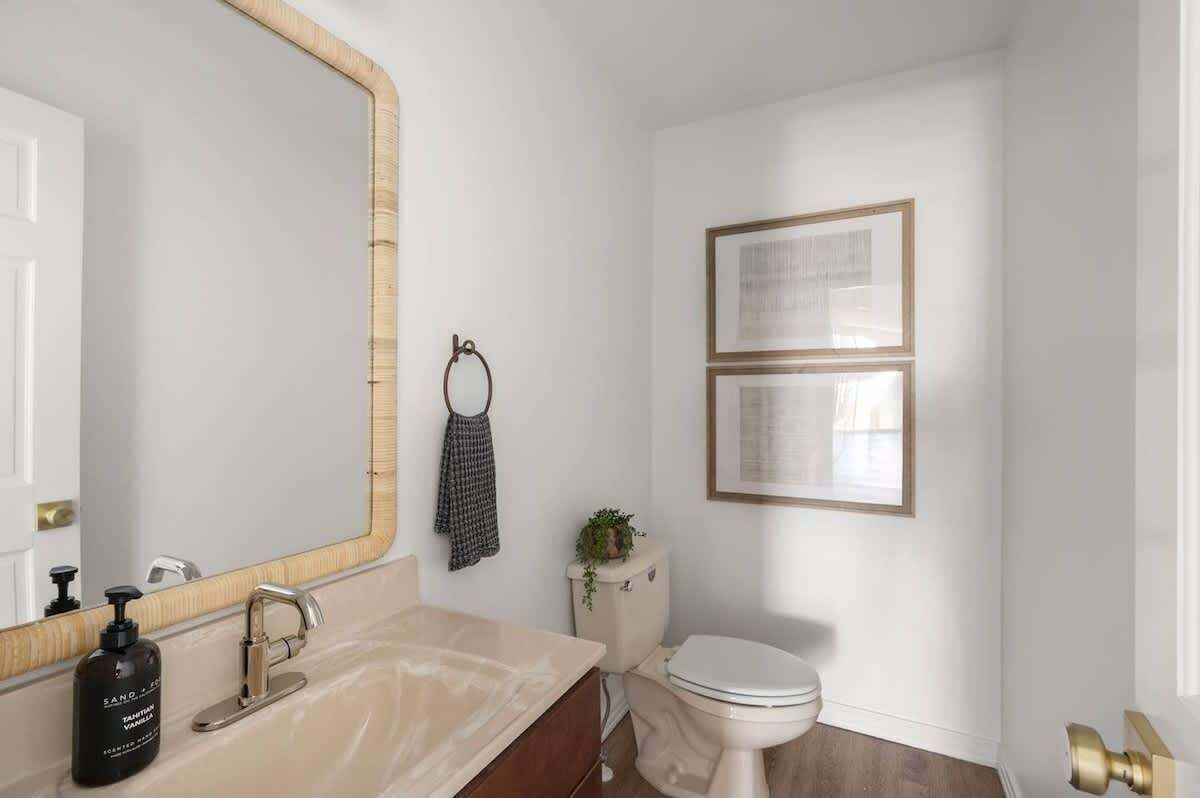 A bathroom with a large mirror, a sink, a toilet, and two framed pictures on the wall.