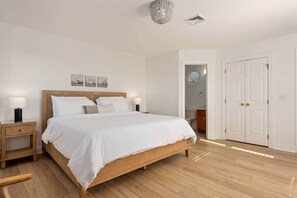A bedroom with a wooden bed, white bedding, two bedside tables with lamps, a chandelier, and a white door. - Oceanfront, Pool & Hot Tub, Game Room, EV Charger (Corolla)