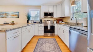 A modern kitchen with white cabinetry, stainless steel appliances, and a granite countertop. - Cozy Soundside Cottage  • Bring Your Dog! (Kill Devil Hills)
