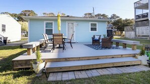 A light blue house with a deck, outdoor furniture, and a small garden. - Cozy Soundside Cottage  • Bring Your Dog! (Kill Devil Hills)