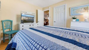 A bedroom with a bed, a television, a chair, and a door leading to another room. - Cozy Soundside Cottage  • Bring Your Dog! (Kill Devil Hills)