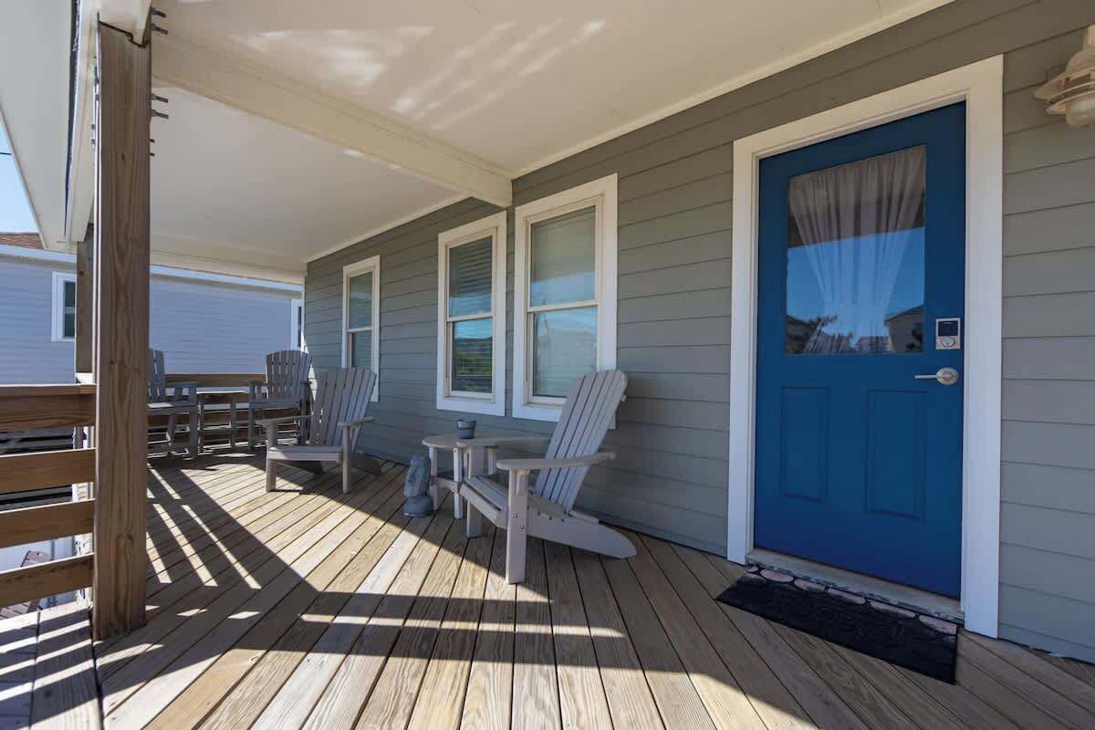 A covered porch with wooden flooring, a blue door, and a seating area with chairs and a table.