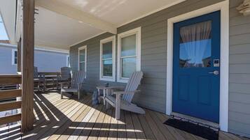 A covered porch with wooden flooring, a blue door, and a seating area with chairs and a table.