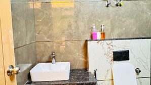 A modern bathroom with a marble sink, a toilet, and a handheld showerhead. - Sky Hotel (Gurugram)