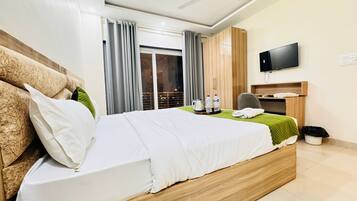 Habitación de hotel con una cama grande, televisor montado en la pared, escritorio con silla y vistas a la ciudad desde la ventana.