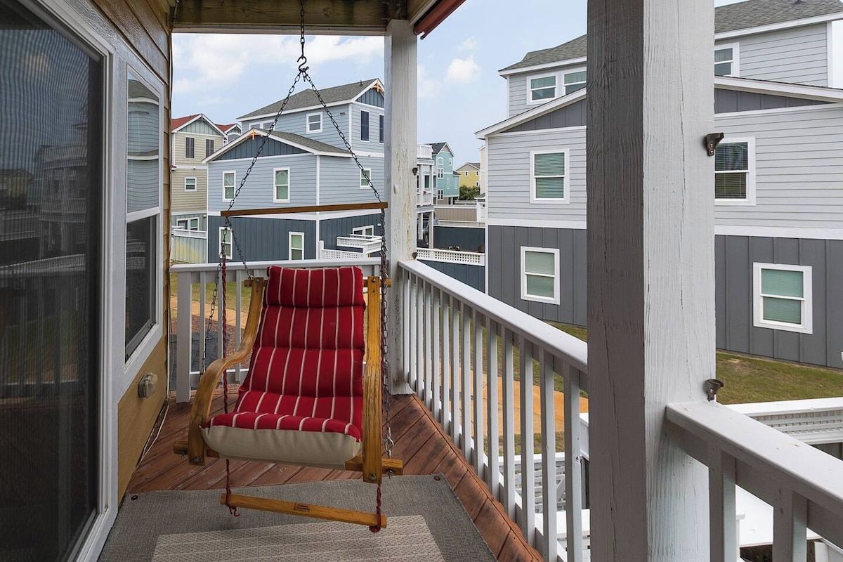 Une véranda avec une chaise suspendue, une balustrade en bois et une vue sur les maisons voisines.