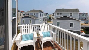 A balcony with two white Adirondack chairs, a wooden deck, and a view of neighboring houses.