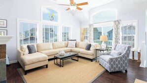 A living room with a beige sectional sofa, a patterned armchair, a coffee table, and a ceiling fan.