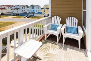 Eine Veranda mit zwei Adirondack-Stühlen und einer Bank, ein Holzdeck und Blick auf eine Reihe von Häusern.