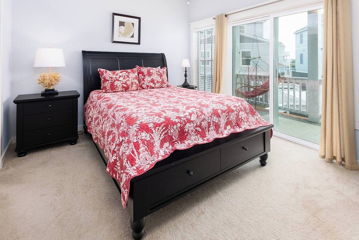 A bedroom with a bed, nightstands, a window with a view, and a door leading to a balcony.